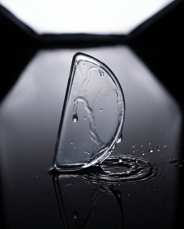 UNBLUR clear prescription lens patch, a wide D shape, resting in water