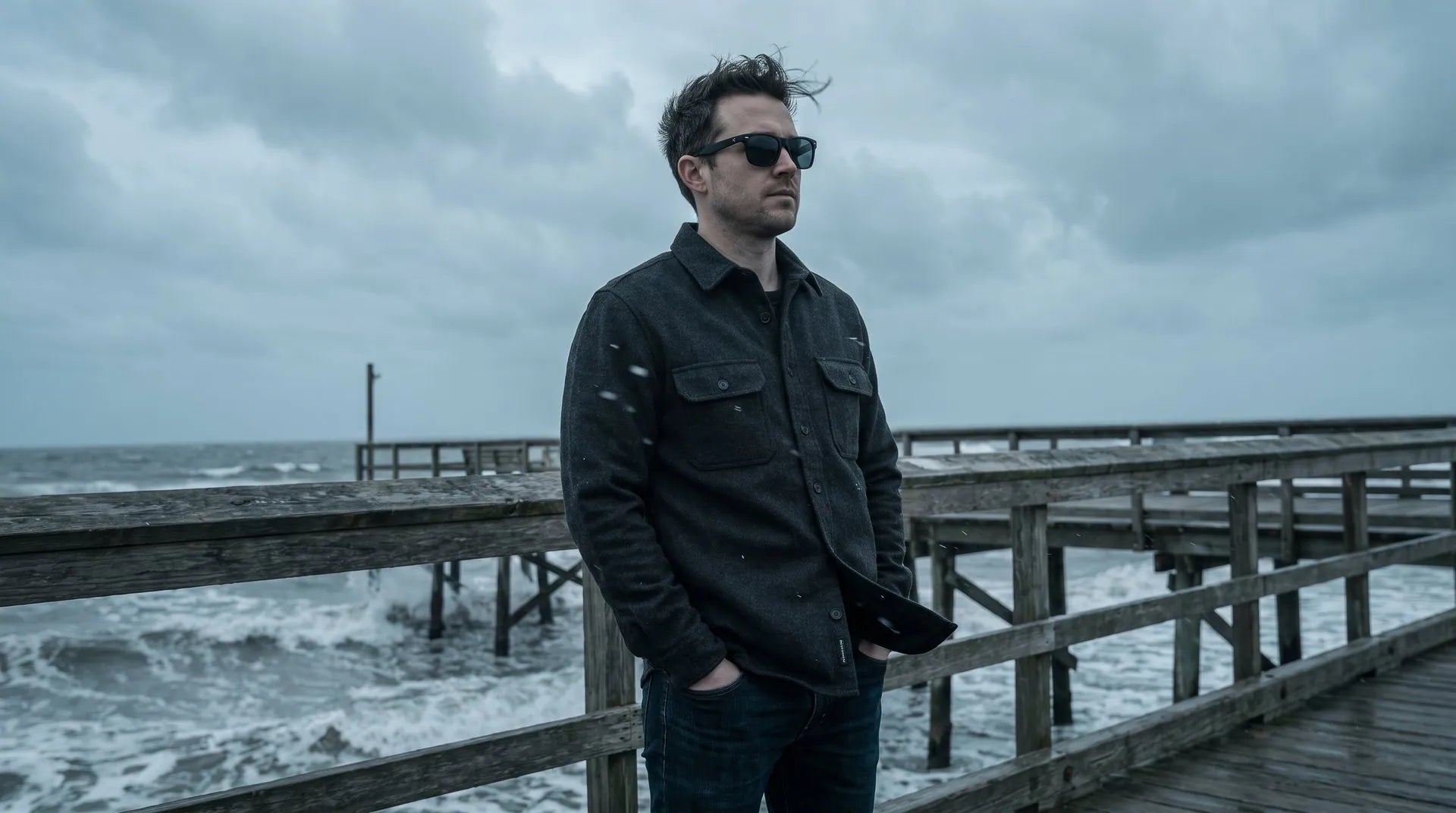 A man in sunglasses on a windy pier